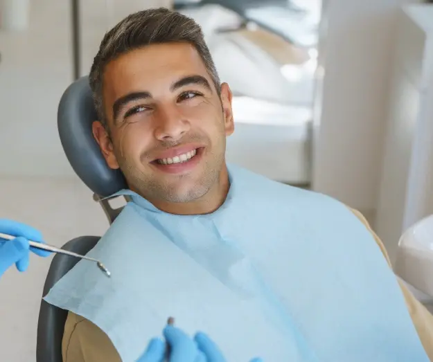 Happy male patient in dental chair receiving treatment at dentist office.