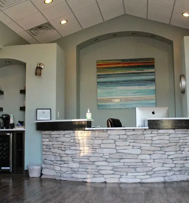 Modern dental practice reception area with curved stone desk and colorful abstract artwork.