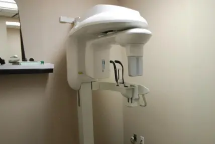 CBCT cone beam scanner mounted on wall in dental office treatment room.