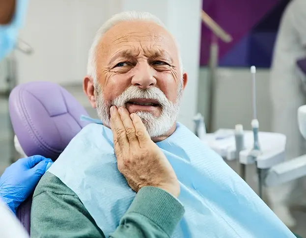 Senior man experiencing tooth pain during dental examination in treatment chair.