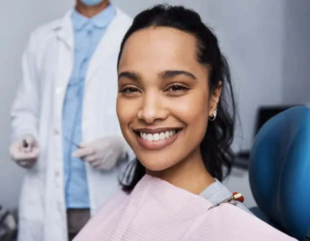Smiling patient in dental chair during endodontic retreatment consultation with dentist.