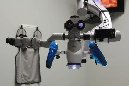 Surgical operating microscope with blue handles used for precise dental procedures and endodontic treatment.
